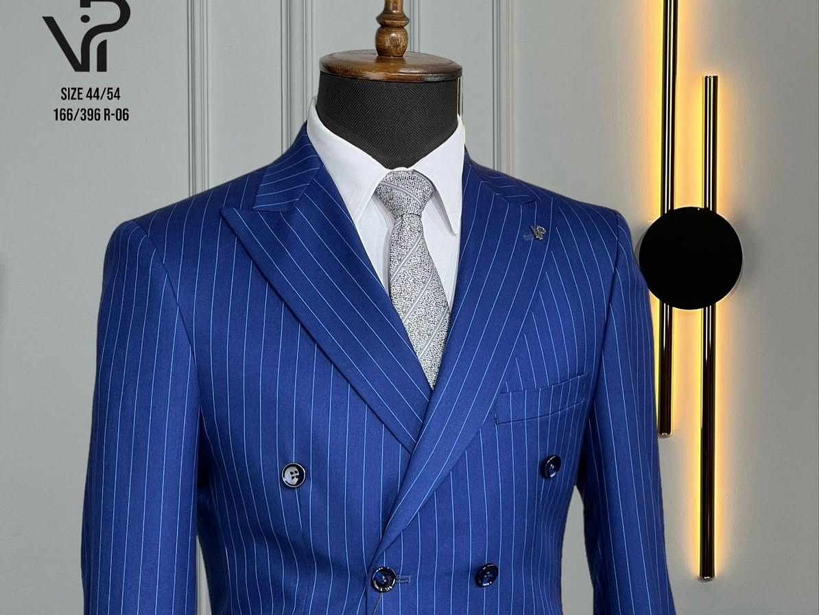 A blue pinstriped double-breasted suit with a light tie is shown on a headless mannequin in a close indoor view.