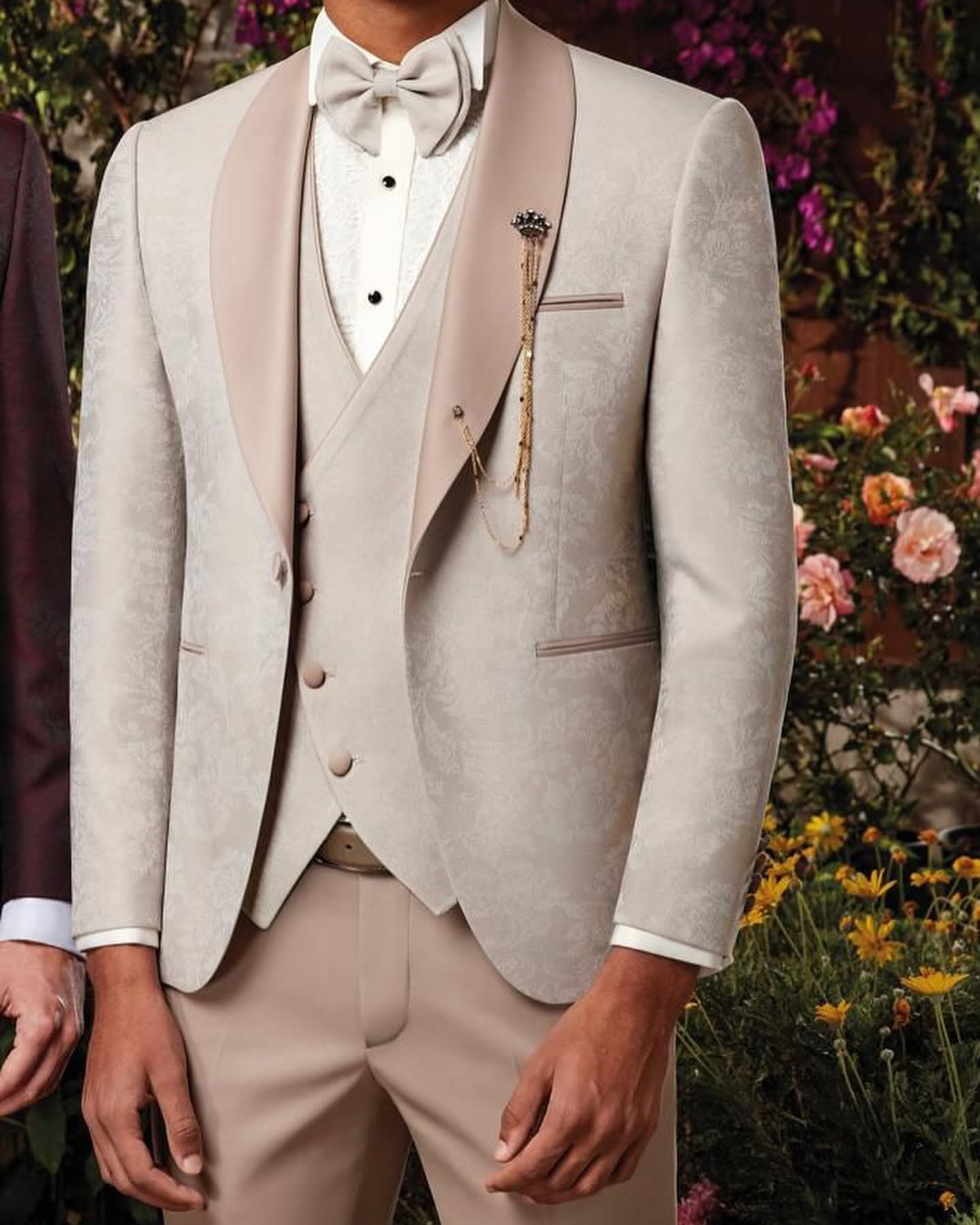 Cropped view of a cream-colored tuxedo and bow tie, with the jacket details framed against a floral background.